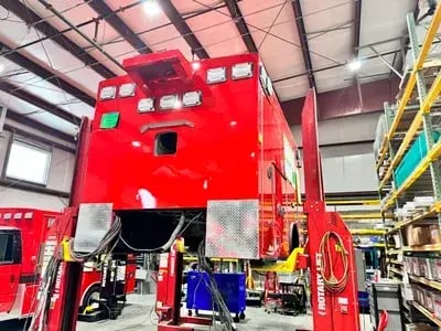 Ambulance patient module raised on hydraulic lifts during the remounting process prior to chassis installation.