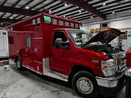 Ambulance undergoing chassis conversion during the remount process with drivetrain and front-end components being installed.