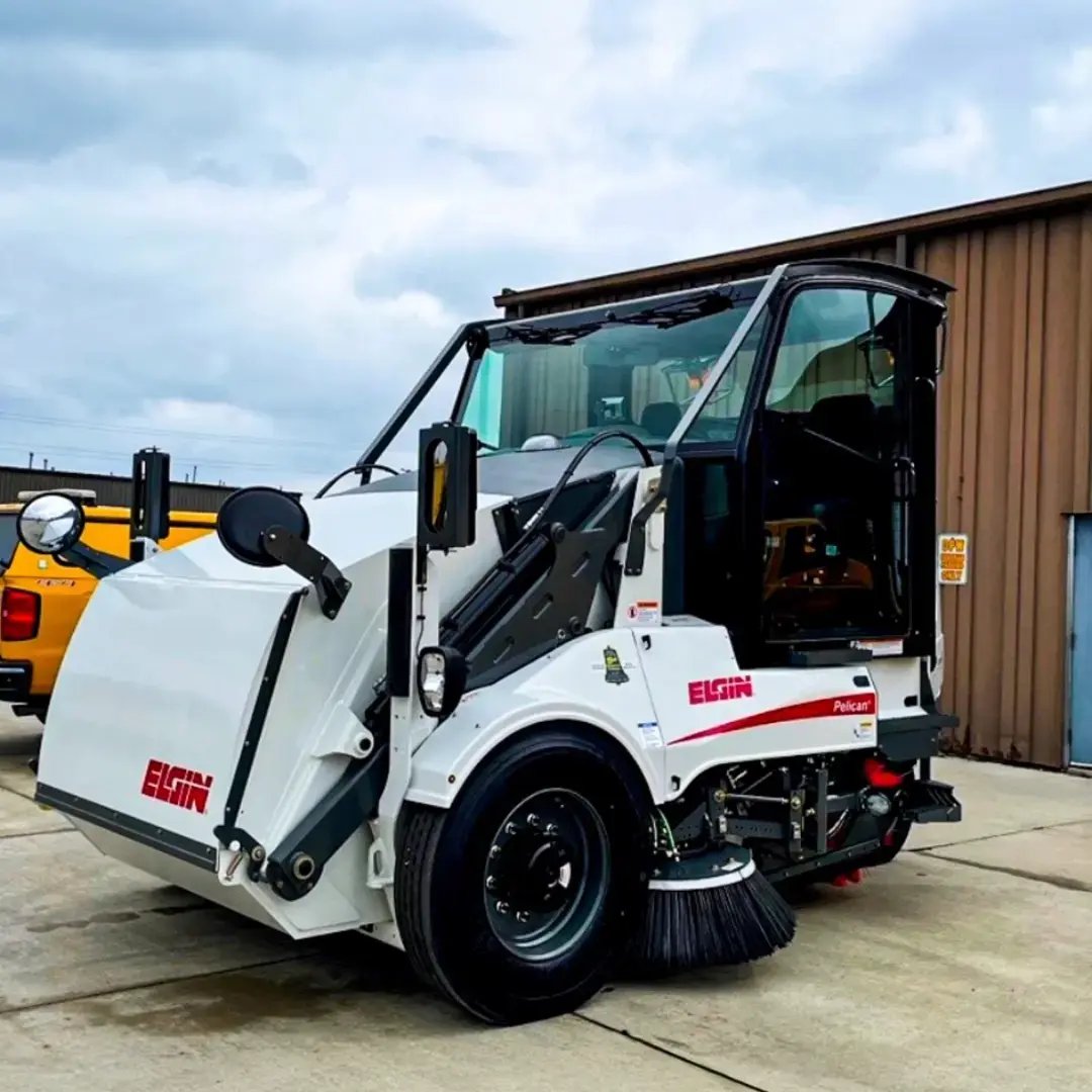 Elgin Pelican street sweeper positioned outdoors, showcasing its compact design, sweeping brushes, and debris collection system for municipal and commercial roadway cleaning.