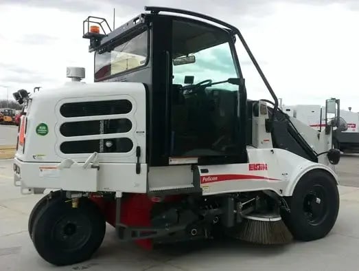 Elgin Pelican compact street sweeper parked at a fleet facility, featuring gutter brooms and a compact design for municipal street sweeping, debris removal, parking lot cleaning, and urban roadway maintenance.