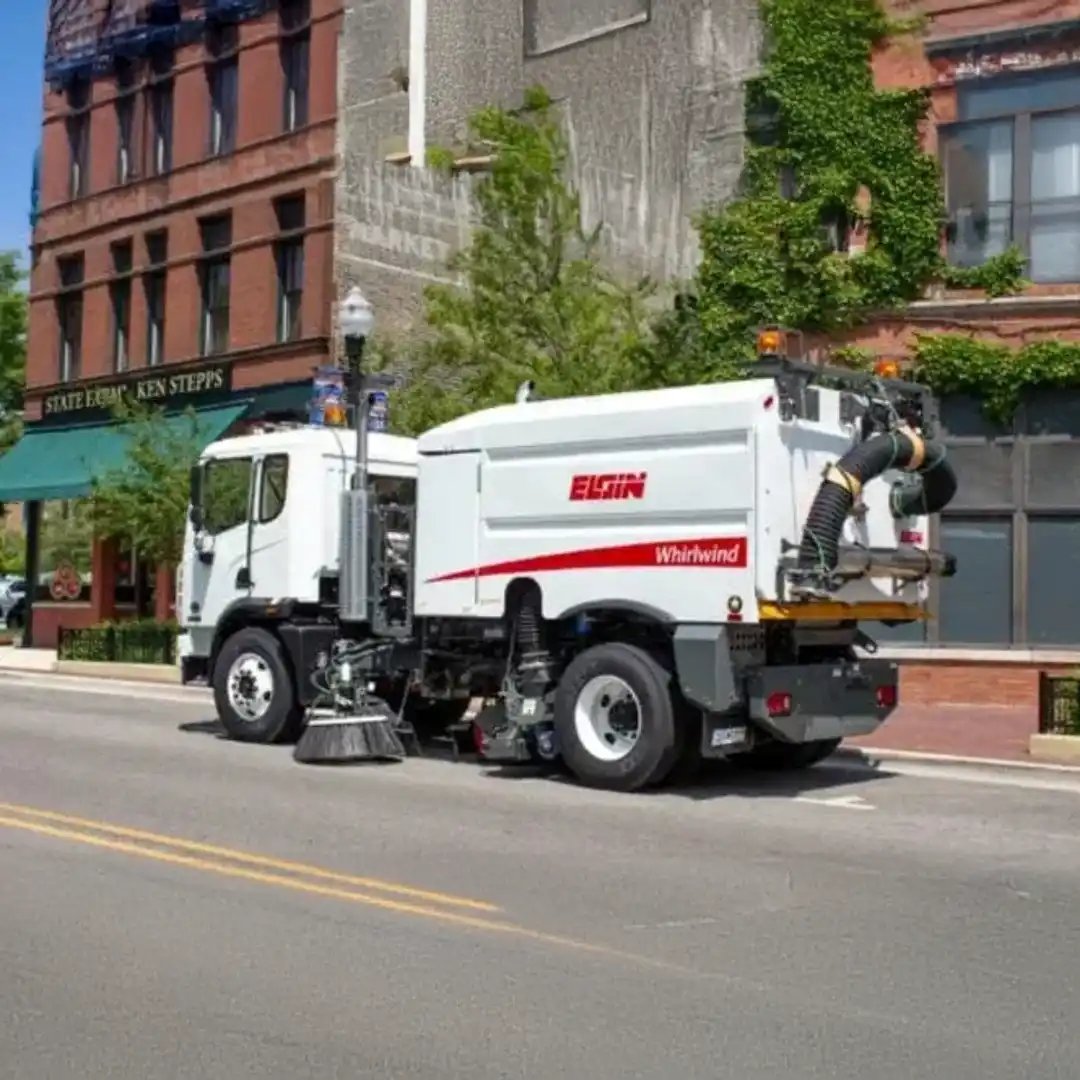 Elgin Whirlwind vacuum street sweeper operating on a downtown city street, featuring powerful vacuum sweeping technology for municipal street cleaning, debris removal, and urban roadway maintenance.