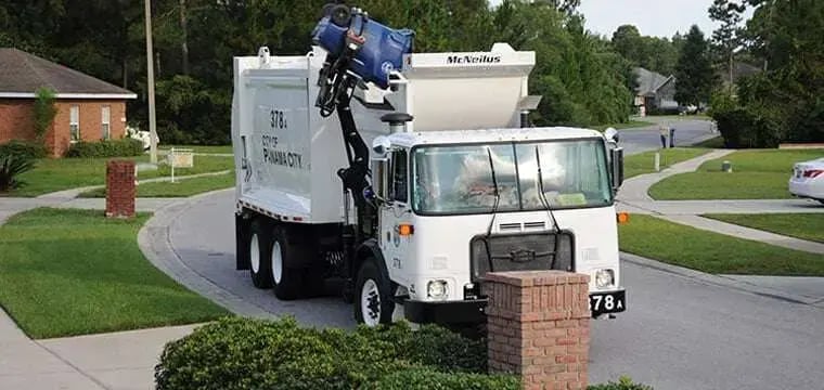 Automated side-loader refuse truck using a mechanical arm to empty a residential waste cart, providing efficient curbside waste collection and sanitation services.