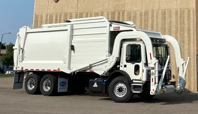 Front-loading refuse truck positioned outdoors, showcasing its automated loading system and high-capacity body designed for commercial waste collection operations.