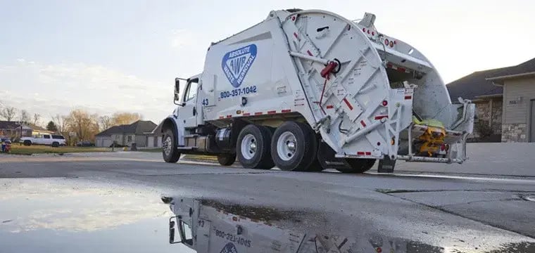 Absolute Waste rear loader garbage truck performing residential curbside trash collection in a suburban neighborhood, featuring a rear-loading compaction system designed for efficient municipal solid waste management.