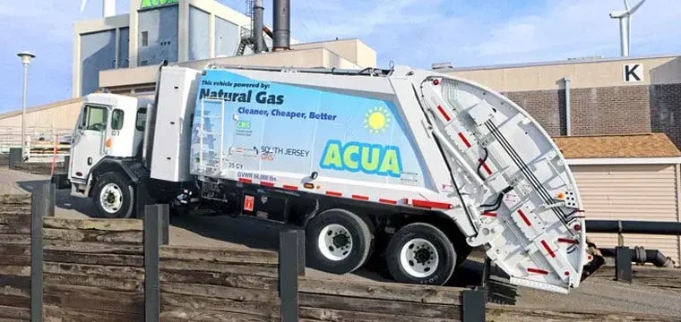ACUA rear loader garbage truck powered by compressed natural gas (CNG), parked at a waste management facility and showcasing sustainable municipal solid waste collection operations.