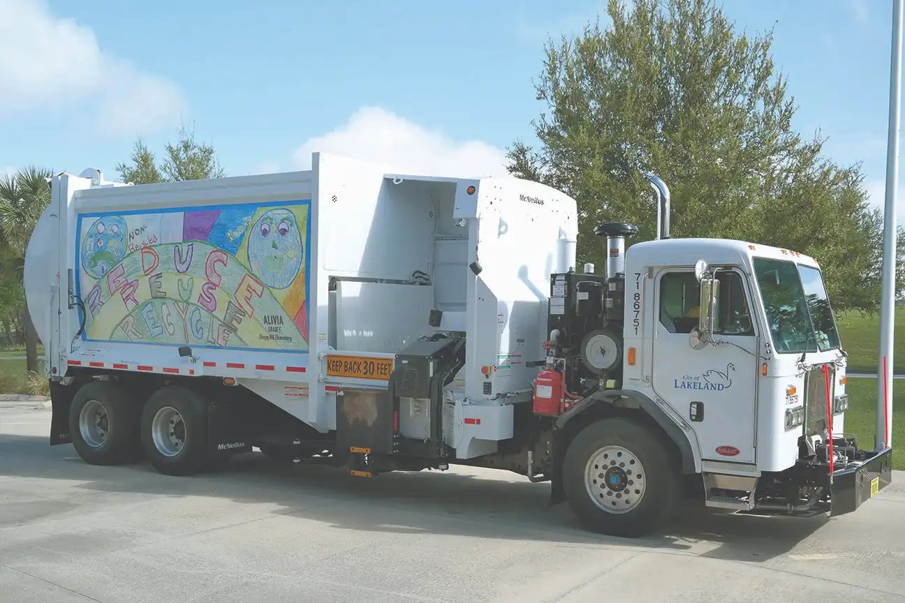 City of Lakeland McNeilus side loader recycling truck featuring a community recycling awareness graphic, parked outdoors as part of a municipal recycling collection program.