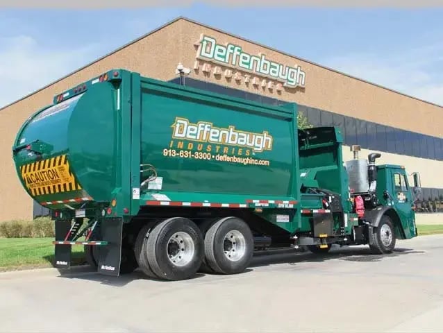 Deffenbaugh Industries automated side loader garbage truck parked outside a company facility, showcasing residential waste collection equipment and automated curbside pickup operations.
