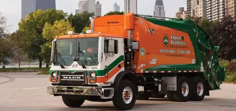 Flood Brothers rear loader garbage truck parked in an urban setting with a city skyline in the background, used for residential and commercial waste collection services.