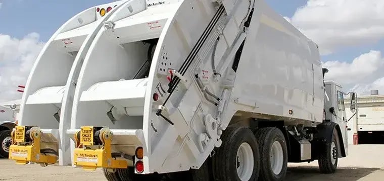 McNeilus split-body rear loader truck featuring separate compartments for recycling and waste collection, designed to improve route efficiency and support dual-stream municipal sanitation operations.