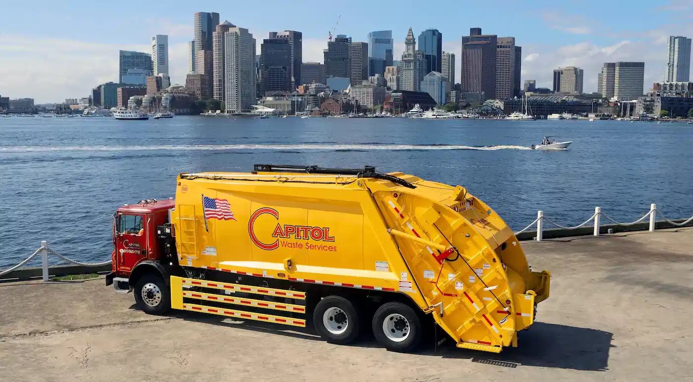 McNeilus rear-loader refuse truck supporting municipal waste collection and sanitation services with a city skyline and waterfront in the background.