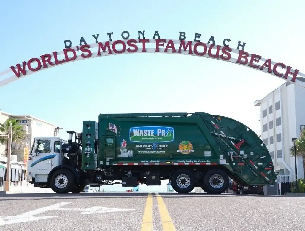 McNeilus rear-loader refuse truck providing municipal waste collection services beneath the Daytona Beach “World’s Most Famous Beach” archway.