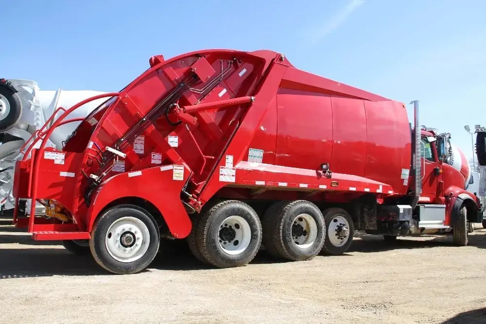 Side view of a red rear loader garbage truck parked outdoors, featuring a high-capacity rear-loading compaction body designed for residential trash collection, municipal sanitation services, and solid waste management operations.