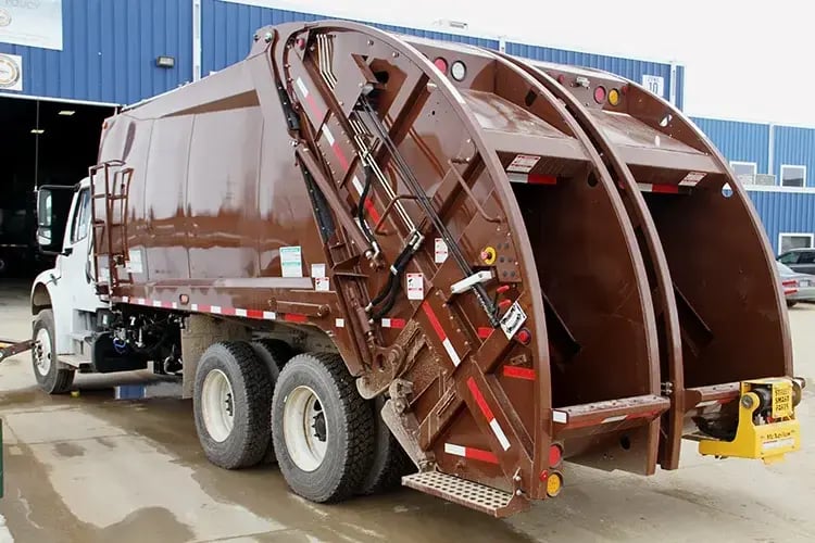 Brown split-body rear loader garbage truck with dual collection compartments, designed for simultaneous waste and recycling pickup to improve municipal collection efficiency and reduce fleet requirements.