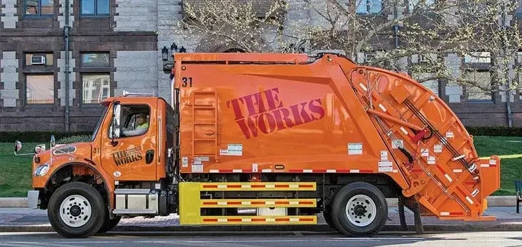 The Works rear loader garbage truck parked along a city street, used for municipal solid waste collection and residential sanitation services in an urban environment.