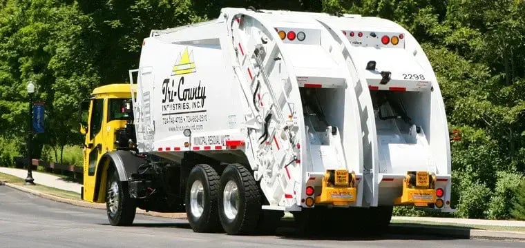 Tri-County Industries split-body rear loader truck with dual compartments for simultaneous recycling and waste collection, operating on a residential route to improve municipal sanitation efficiency and sustainability.