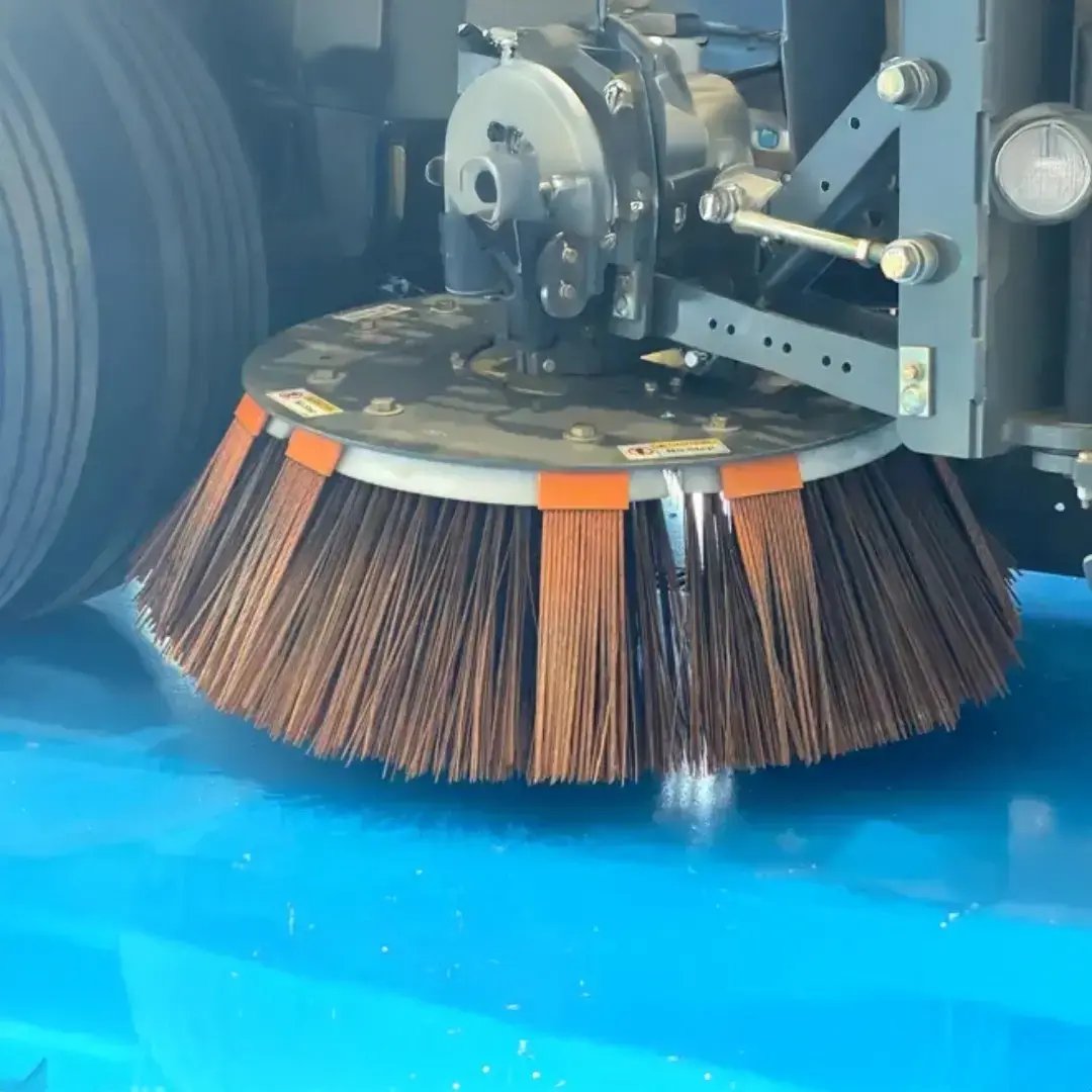 Close-up of a street sweeper brush assembly, highlighting the sweeping bristles and mechanical components inspected during detailed equipment service and maintenance.