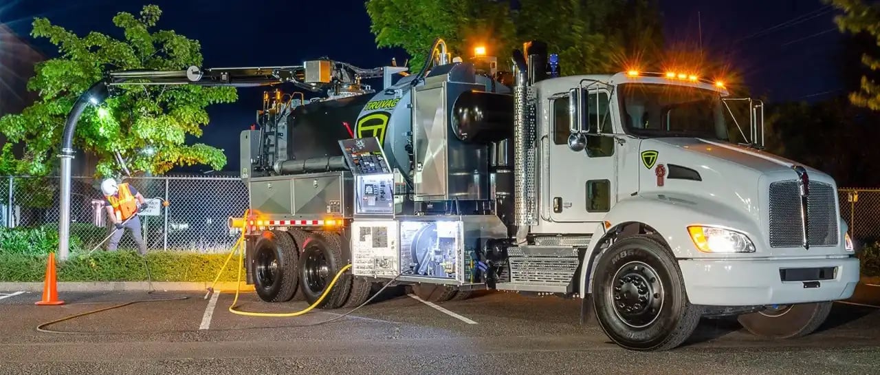 TRUVAC hydro excavation vacuum truck performing nighttime utility excavation with an extended vacuum boom while utility workers safely expose underground infrastructure using non-destructive hydro excavation technology.