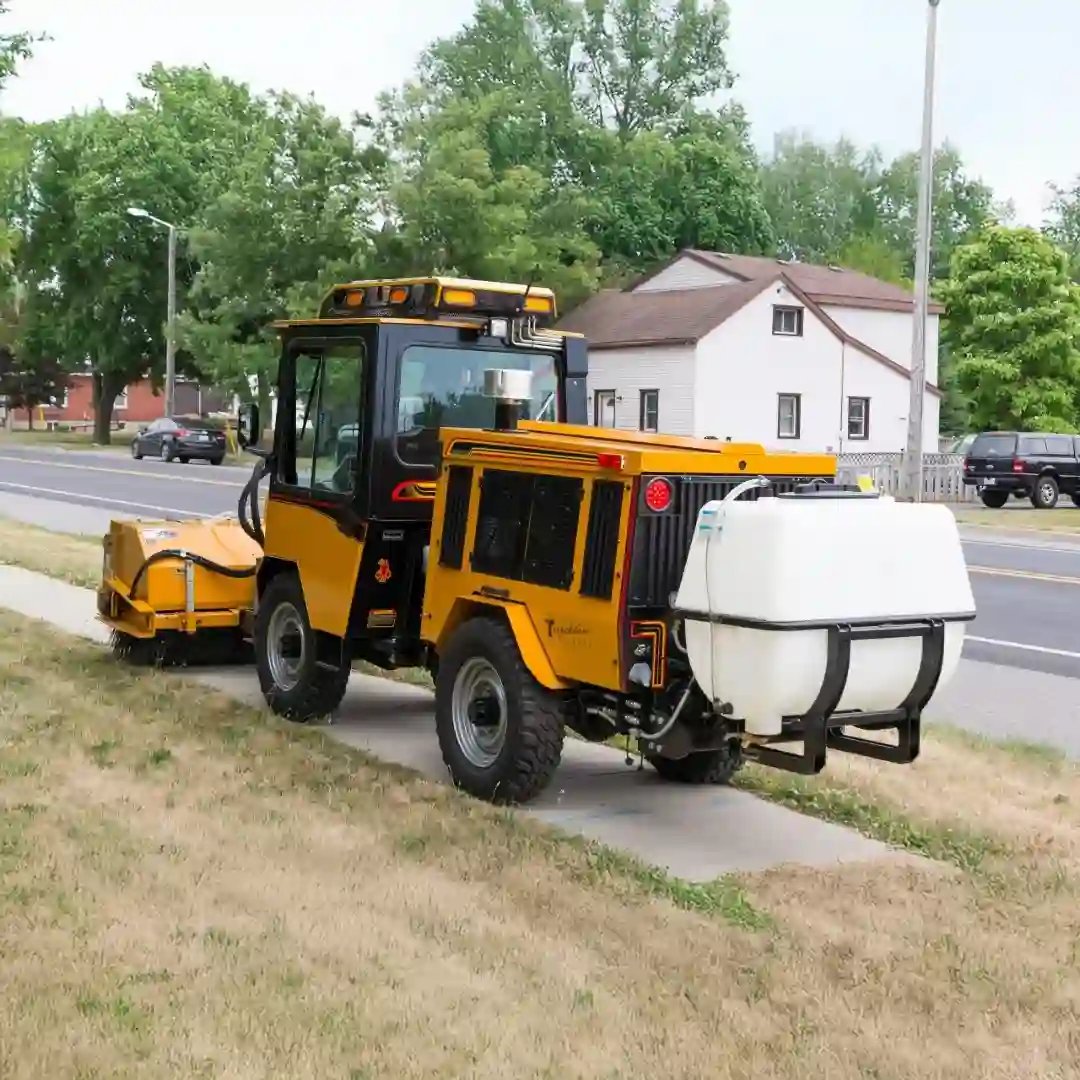 Trackless MT7 municipal tractor equipped with a rear liquid brine sprayer and front boom sprayer for anti-icing and deicing sidewalks, trails, and public spaces.