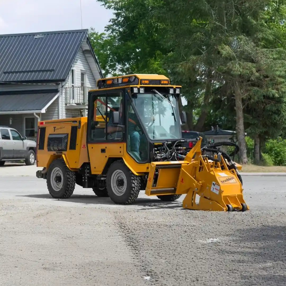 Trackless MT7 municipal tractor with a front-mounted cold planer attachment milling and removing damaged asphalt for road, sidewalk, and pavement repair applications.