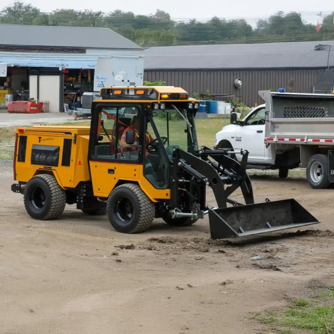 Trackless MT7 municipal tractor equipped with a front-end loader bucket for moving soil, gravel, mulch, snow, and other materials during municipal maintenance.
