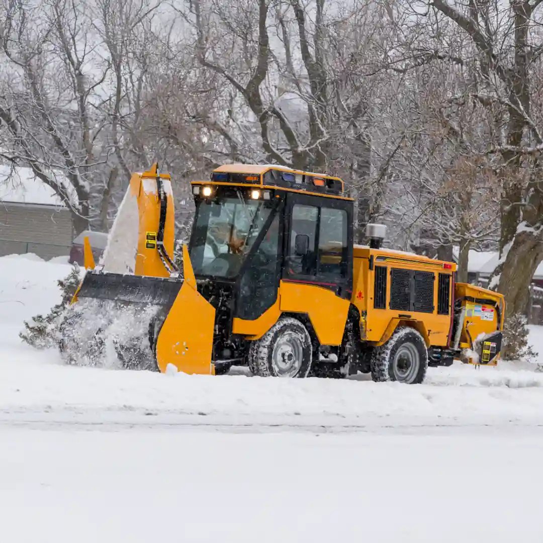 Trackless MT7 municipal tractor operating with a front-mounted ribbon snow blower to clear heavy snow from roads, sidewalks, and public spaces.