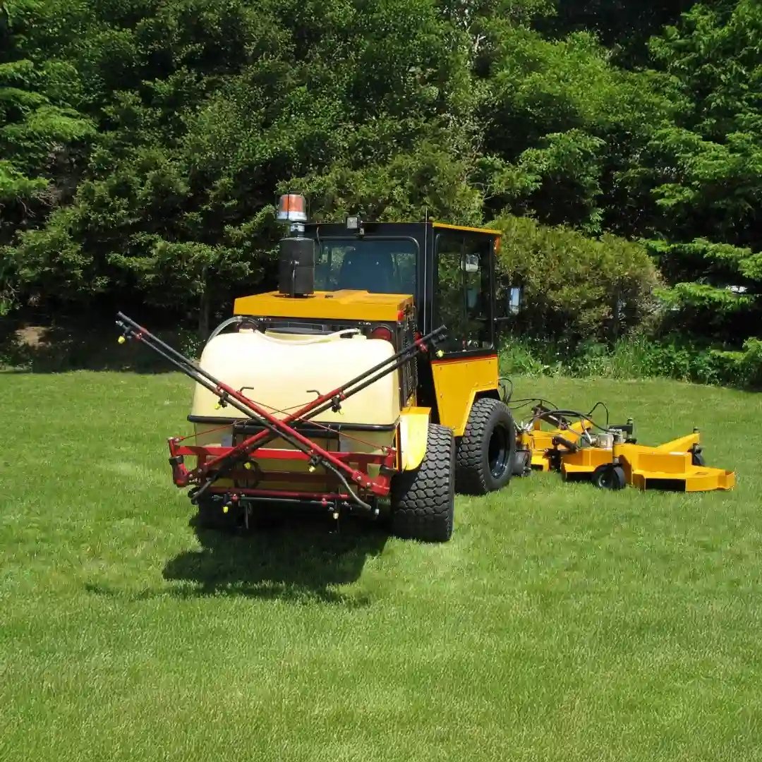 Trackless MT7 municipal tractor equipped with a rear liquid sprayer and front mower for turf maintenance, weed control, and grounds management.