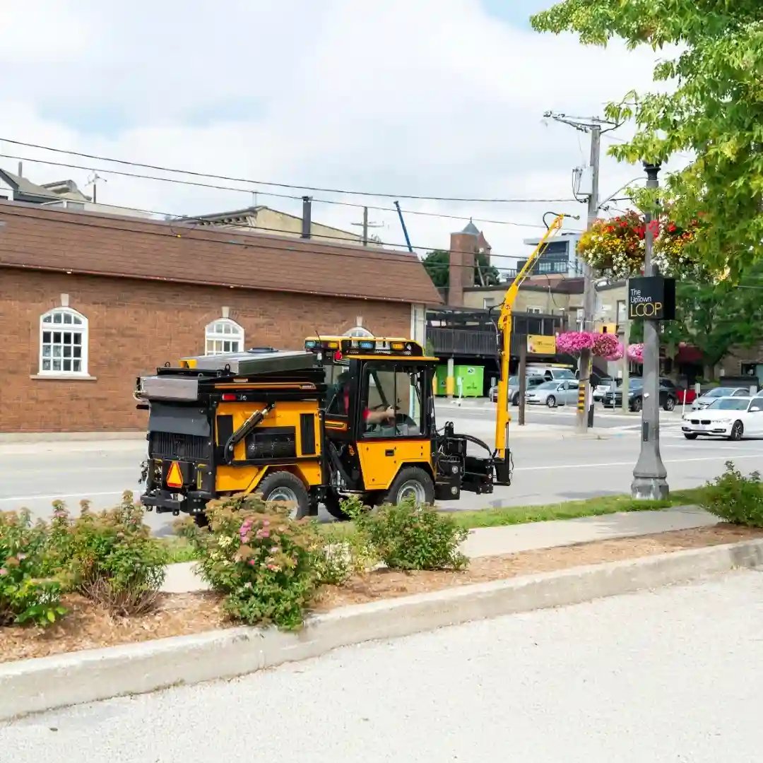 Trackless MT7 municipal tractor equipped with a hydraulic watering arm for irrigating hanging flower baskets, planters, and streetscape landscaping.