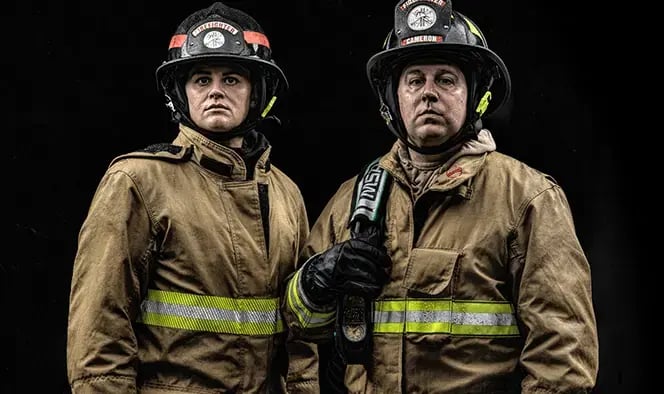 Two firefighters wearing turnout gear, fire helmets, and respiratory protection equipment during firefighting operations.