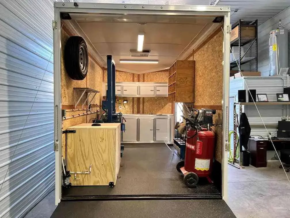 Interior of a mobile hydraulic service trailer with storage cabinets, workbench, air compressor, and repair equipment.