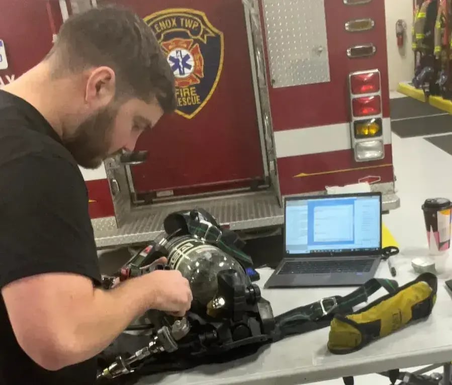 Technician performing flow testing and maintenance on an MSA SCBA unit using diagnostic software inside a fire station.