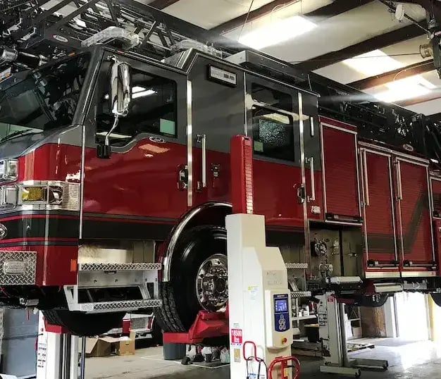 Pierce fire apparatus undergoing maintenance on a vehicle lift inside a certified emergency vehicle service facility.