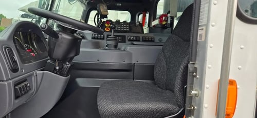 Driver cab interior of a McNeilus Atlantic 40-yard front loader garbage truck with steering wheel and operator controls.