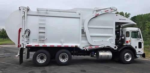 Passenger side profile of a McNeilus Atlantic 40-yard front load refuse truck.