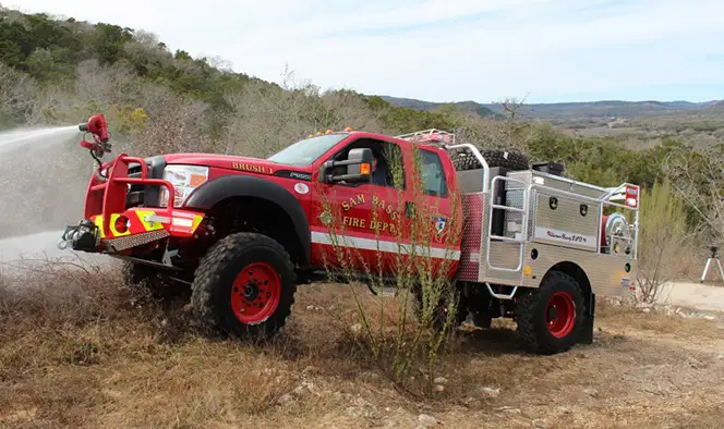 Right-side view of a Skeeter step-side brush truck with off-road tires, equipment compartments, and emergency warning lights.