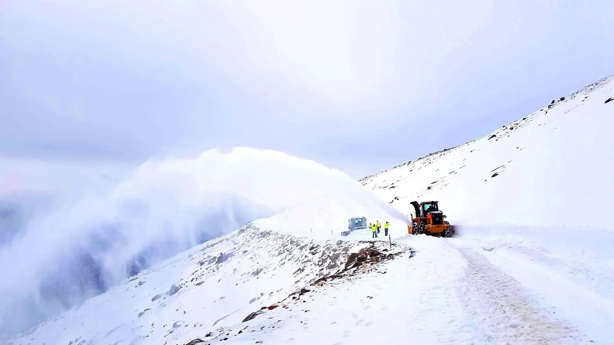 Heavy-duty snow removal equipment clearing deep snow from a mountain roadway, using a high-capacity snow blower to maintain safe winter travel in extreme weather conditions.