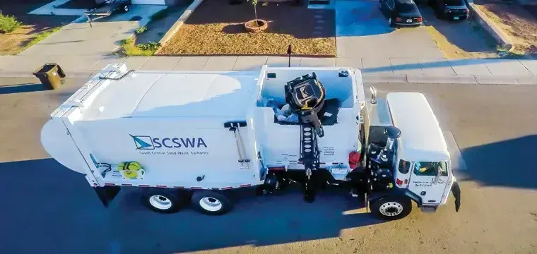 Automated side-loader refuse truck collecting residential waste carts in a neighborhood, providing efficient curbside waste collection and sanitation services.