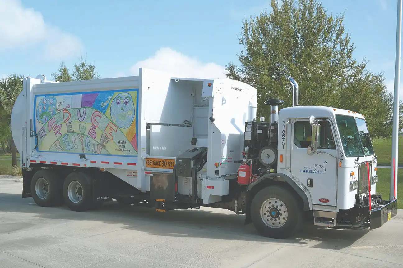 City of Lakeland McNeilus side loader recycling truck featuring a community recycling awareness graphic, parked outdoors as part of a municipal recycling collection program.
