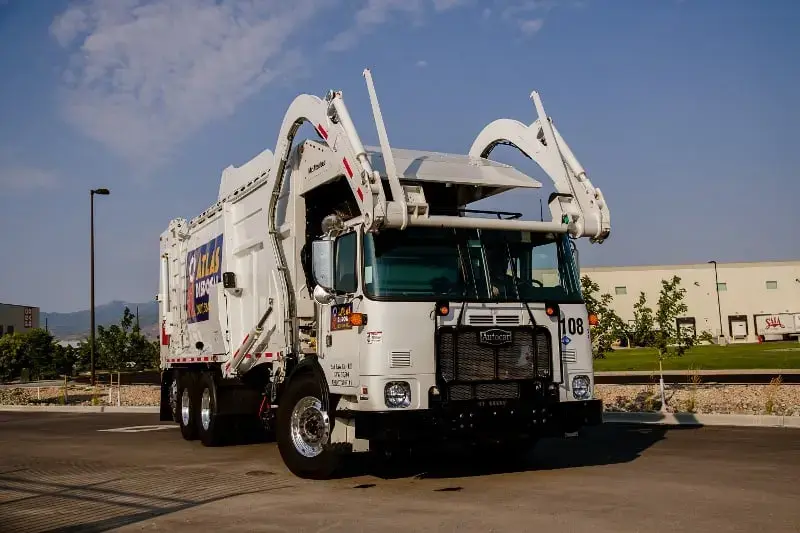Front loader garbage truck equipped with automated lifting arms, parked in an industrial area and designed for commercial waste and dumpster collection operations.