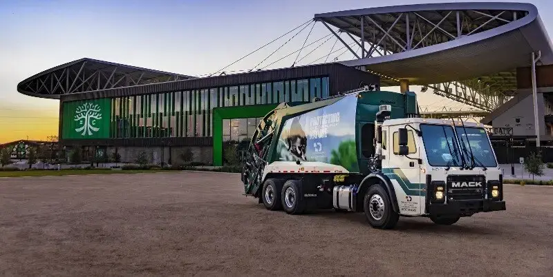 McNeilus rear-loader refuse truck parked outside a municipal facility, showcasing reliable waste collection equipment for sanitation and recycling operations.