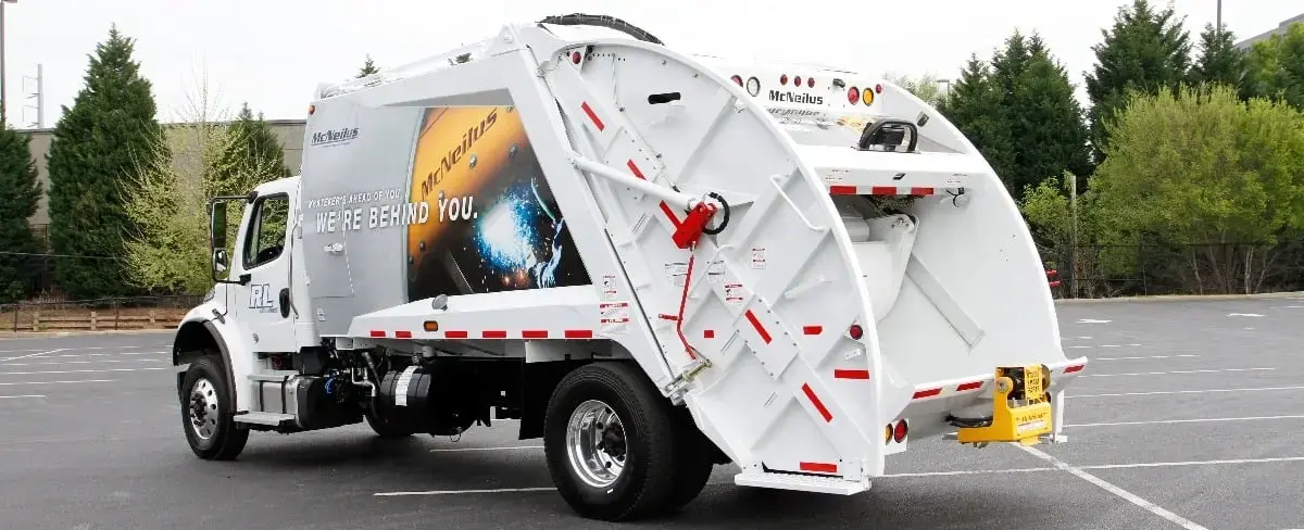 McNeilus rear loader garbage truck parked in a lot, featuring a high-capacity rear-loading hopper and compaction system designed for residential and municipal solid waste collection operations.