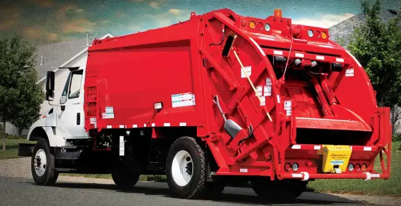 Red rear loader garbage truck parked in a residential neighborhood, featuring a rear-loading hopper and compaction system designed for municipal solid waste and residential trash collection.