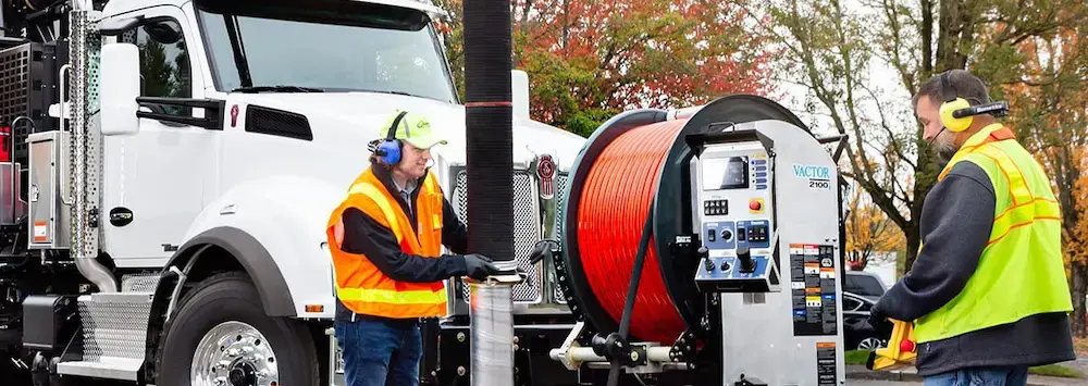 Workers wearing Sonetics wireless headsets while operating sewer and wastewater equipment, enabling clear communication and coordinated field operations in demanding environments.