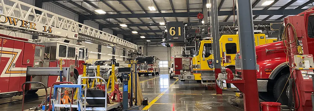 Emergency vehicle service facility with fire apparatus, ambulances, and maintenance equipment inside a repair bay.