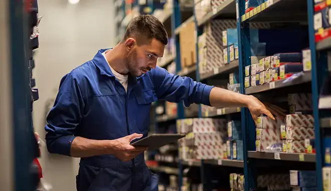 Technician reviewing equipment components on warehouse shelving to identify parts for return, replacement, or service support.